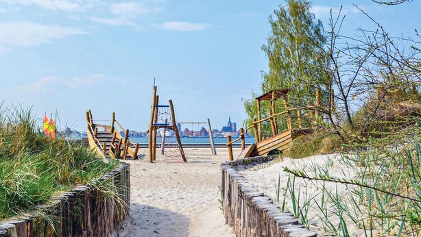 A beach path leading to a wooden structure with a netted swing set, surrounded by sand and vegetation. - Ferienwohnung Altefähr (Altefähr/Rügen)