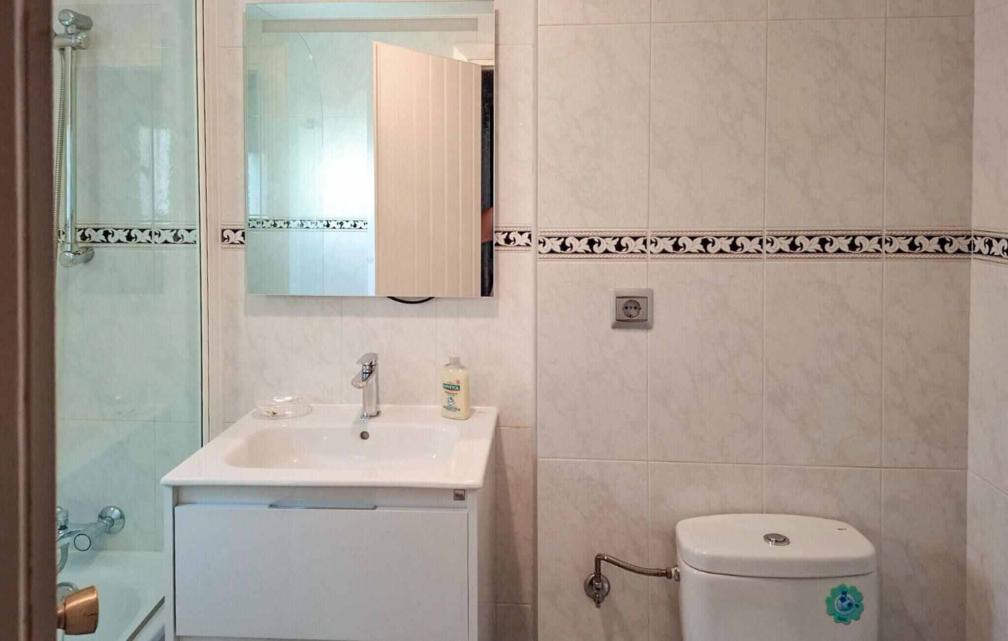 Une salle de bain avec une douche à parois de verre, un lavabo blanc avec un miroir au-dessus et des toilettes décorées d’un autocollant.