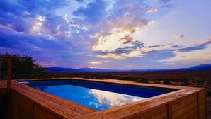 Una piscina infinita de madera con vista despejada a un paisaje desértico y montañas al fondo.