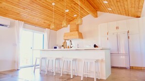 Una cocina moderna con armarios blancos, una isla central con taburetes, lámparas colgantes de mimbre y horno empotrado.