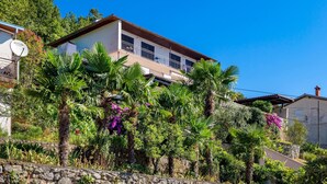 A two-story house with a balcony, surrounded by lush greenery and flowering plants. - Stunning apartment in Opatija with WiFi (Opatija)