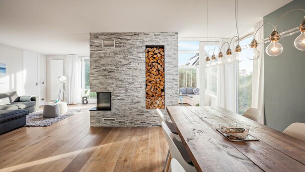 Un salon moderne doté d’une cheminée en pierre, de planchers en bois et d’un coin repas avec une table et des chaises en bois.