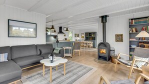 A modern living room with a sofa, coffee table, and a fireplace. There is a dining area with chairs and a table.