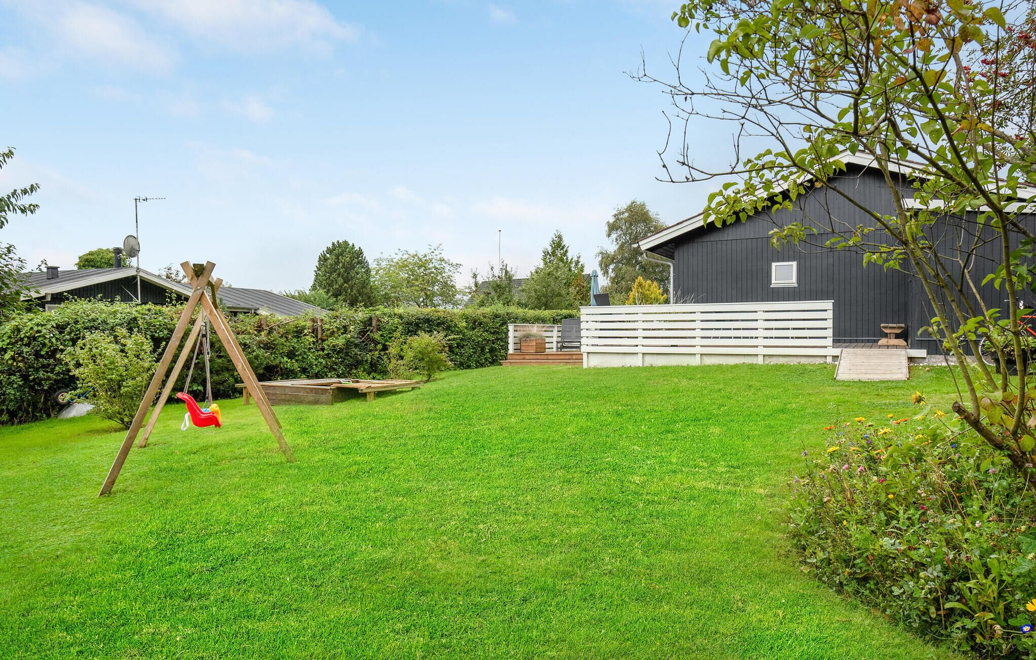 A backyard with a swing set, a wooden deck, and a fenced area.