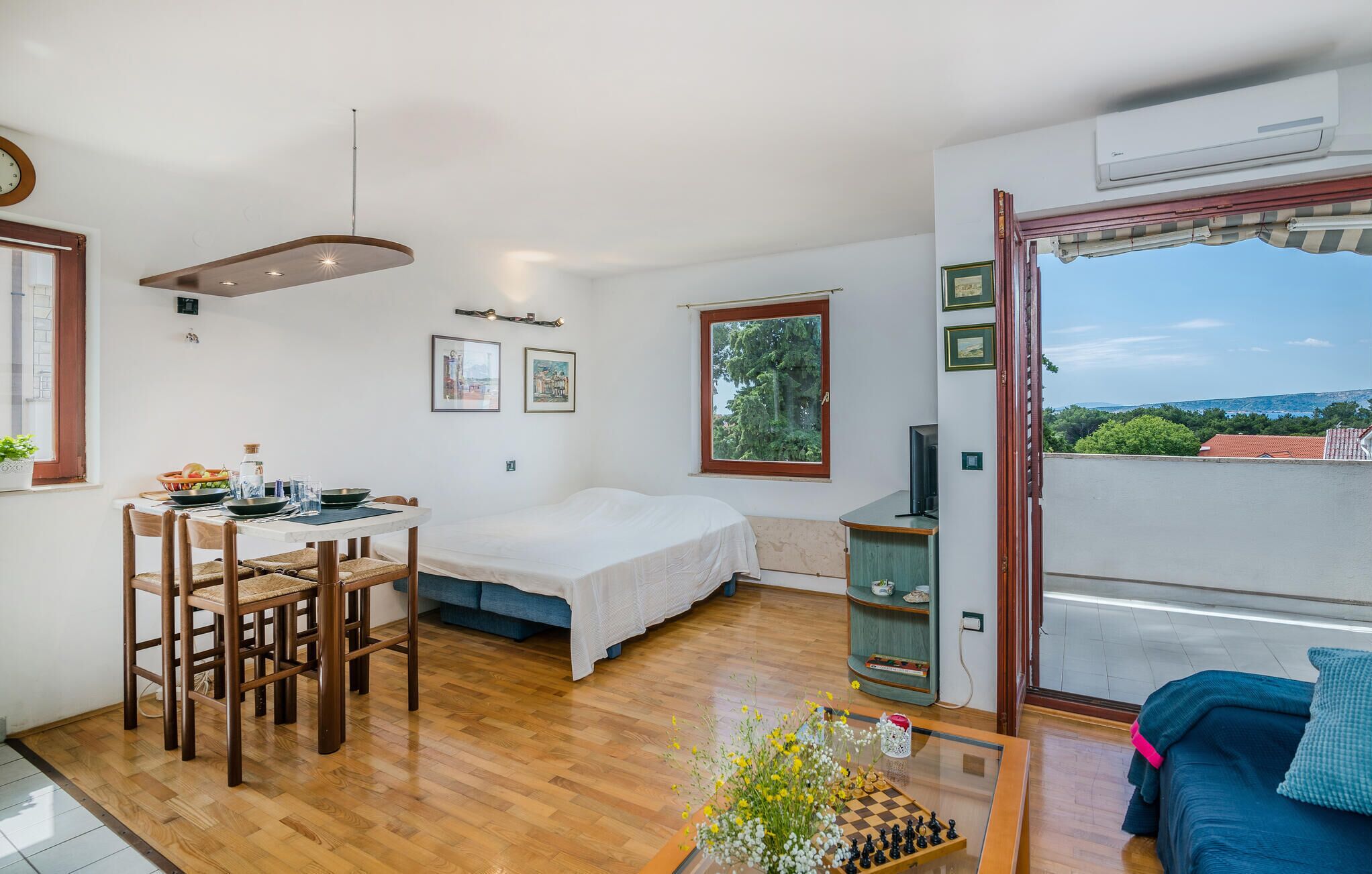 Quarto compacto com cama, mesa de jantar com cadeiras, pequena cozinha e varanda com vista.