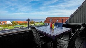 A terrace with a table and chairs, overlooking a coastal view with houses and a swimming pool. - Gorgeous apartment in Gudhjem with WiFi (Gudhjem)