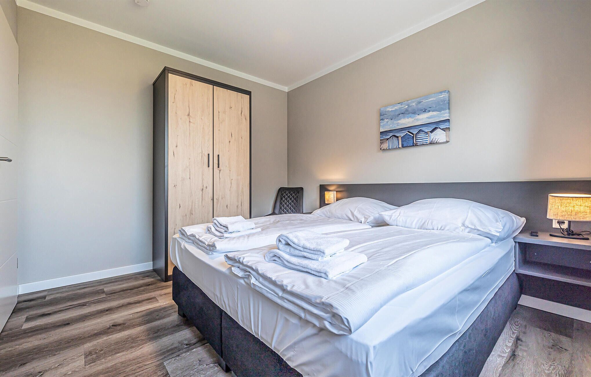 A hotel room with a bed, a wardrobe, a painting, a nightstand, and a lamp.