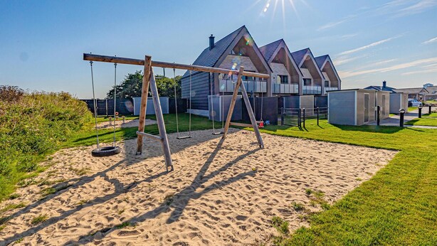A residential area with a swing set, a sandy play area, and modern houses with pitched roofs.