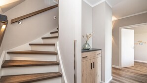 A staircase with wooden steps and a black top rail, leading to a room with a wooden cabinet and a vase of dried flowers on a black countertop.