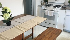 Eine Küche mit weißem Herd, einer Spüle und Schränken. Es gibt einen Tisch mit einer Bank und einem Blumentopf.