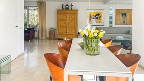 Un coin repas avec une table blanche, des chaises orange et un vase de fleurs.