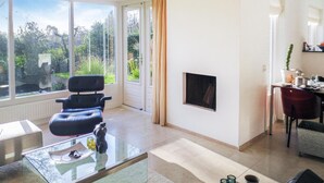 Un salon spacieux doté d’une grande fenêtre, d’un canapé en cuir noir, d’une table basse en verre et d’un téléviseur à écran plat fixé au mur.