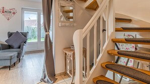 Eine Treppe mit Holzboden und weißen Geländern, ein graues Sofa mit Kissen, ein kleiner Tisch und ein Fenster mit Vorhängen.