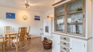 Ein Essbereich mit einem runden Tisch und Korbstühlen, einem weißen Schrank mit Glastüren sowie einem Kompass an der Wand.