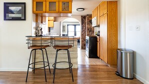 A kitchen with wooden cabinets, a stainless steel trash can, and a bar area with stools. - 5-Star Lux Modern Cabin in DT Fruita ❊ Dog Friendly❊ (Fruita)