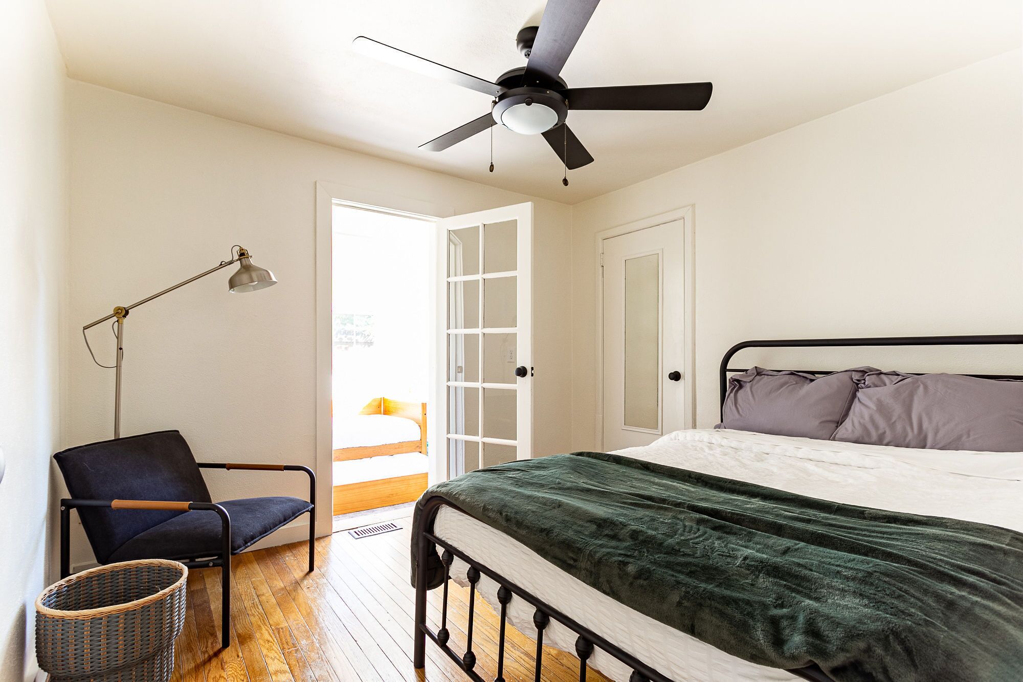 A bedroom with a bed, a chair, a floor lamp, and a ceiling fan.