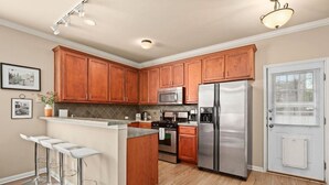 A modern kitchen with wooden cabinets, stainless steel appliances, and a bar area. - 8th #B xxxxxxxxxxxxx (Austin)