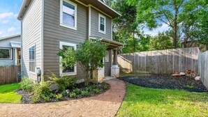 A two-story house with a covered porch, a landscaped garden with a curved pathway, and a wooden fence. - 8th #B xxxxxxxxxxxxx (Austin)