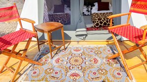 Uma tenda com uma cama, duas cadeiras de madeira e um tapete estampado.