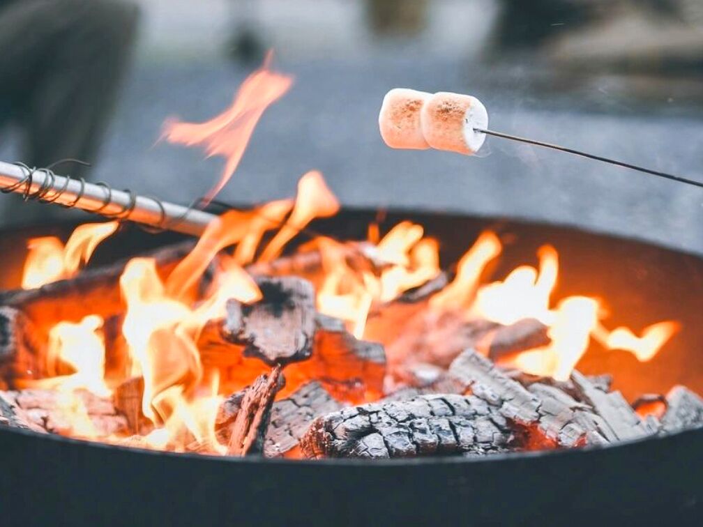 A close-up of a campfire with two marshmallows roasting on a stick.
