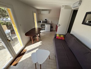 A compact living space with a dining table, sofa, kitchenette, and a sliding door leading to an outdoor area.
