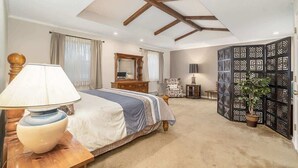 A bedroom with a bed, bedside table, lamp, dresser, mirror, curtains, and a decorative partition.