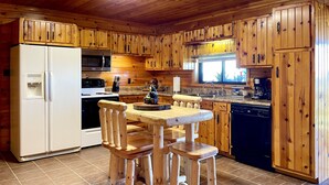 Eine Küchenzeile im Chalet-Stil mit Kühlschrank, Mikrowelle, Herd und einem Holztisch mit Stühlen.