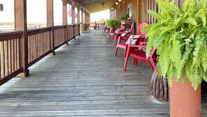 Eine überdachte Holzterrasse mit roten Stühlen, Kübeln mit Farne, Holzgeländern und großen Fenstern.