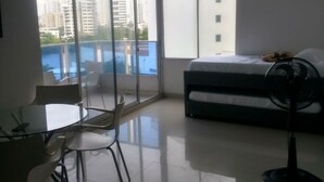 Une chambre d’hôtel moderne dotée d’un grand balcon, d’un lit, d’une table avec des chaises et d’un ventilateur sur pied.