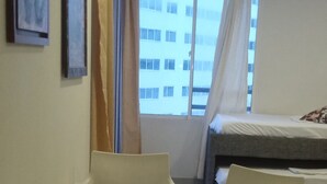 Une pièce avec une table en verre entourée de chaises, un lit avec un matelas blanc et une fenêtre avec des rideaux.