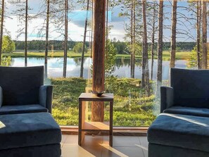 Een kamer met twee stoelen gericht op een groot raam met uitzicht op een meer en bomen.