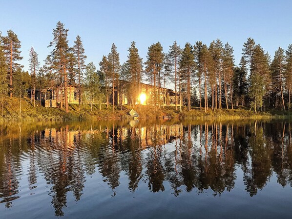 A cabin surrounded by tall trees and a calm lake reflecting the structure.