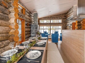A log cabin interior with a dining area, stone fireplace, and large windows.