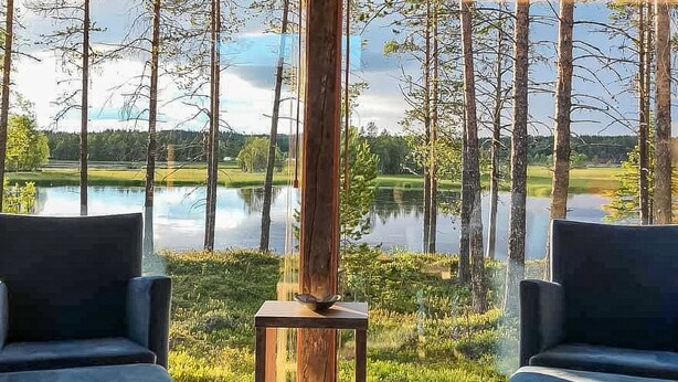 Una habitación con dos sillas azul oscuro frente a un ventanal con vistas a un lago y un bosque.