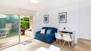 A modern living room with a blue sofa, white chairs, a desk, and a glass door leading to a garden. - Tramuntana by Interhome (L'Escala)