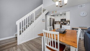 Une cuisine moderne avec des meubles blancs, une table à manger en bois et un escalier menant à un autre niveau.