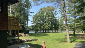 Une terrasse en bois avec des meubles d’extérieur, un mur en pierre et une vue sur un lac entouré d’arbres.