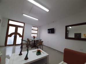 A room with a dining table, chairs, a TV mounted on the wall, and a large mirror.