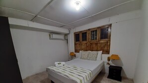 Une chambre à coucher avec un lit, une table de chevet, une fenêtre avec des volets en bois et un luminaire au plafond.