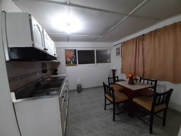 Une cuisine de taille réduite avec des meubles blancs, une cuisinière et une table à manger avec des chaises.