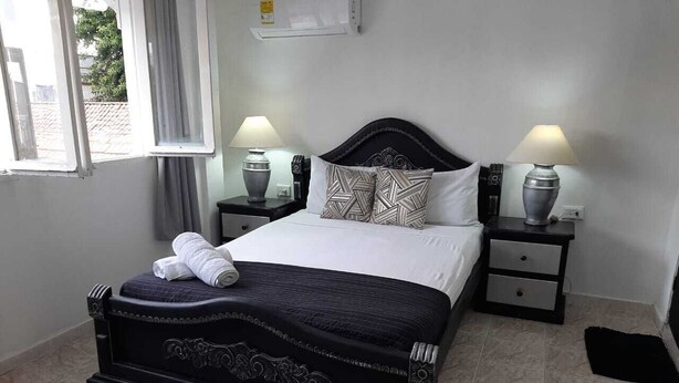 A bedroom with a black headboard, white bedding, two bedside lamps, and a window with curtains. - 1G3-2 Apartamento en la Ciudad Antigua (Cartagena)