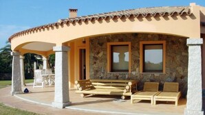 A covered outdoor seating area with stone walls and a tiled roof, featuring two windows and a stone pillar. - Rei Sole (REI305) by Interhome (Costa Rei)