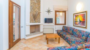 A living room with a stone wall, a fireplace, a colorful sofa, and a television. - Rei Sole (REI305) by Interhome (Costa Rei)