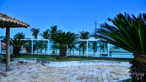 Un espace extérieur aménagé avec une allée pavée, des palmiers, un coin salon couvert et une vue sur la plage.
