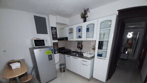 A compact kitchen with white cabinets, a microwave, a small dining table, and a trash bin. - 1G2-3 Apartamento en la ciudad Antigua (Cartagena)