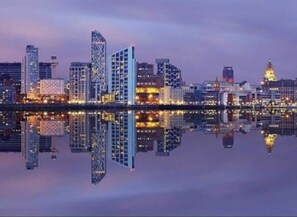 Une vue sur les gratte-ciel d’une ville au crépuscule, les bâtiments modernes se reflétant dans l’eau.