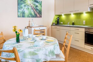 Un coin repas avec une table dressée pour quatre personnes, un vase rempli de fleurs et une cuisine avec un plan de travail vert.