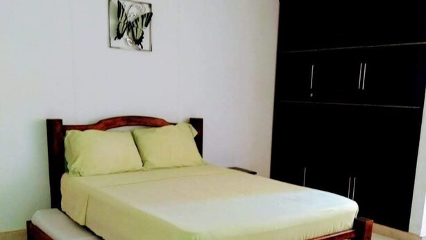 A single bed with a wooden frame and a mattress, a small bench at the foot of the bed, a black wardrobe, and a glass coffee table. - 2C19 Apartamento Cartagena frente al mar (Cartagena)