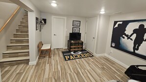 A room with a wooden staircase, a flat-screen TV, a 'Packers' themed rug, and a wall mural. - Packer themed, renovated 3 bedroom, 2 1/2 bath home- Lambeau Field 16 min walk. (Green Bay)