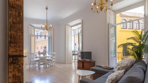 A spacious living area with a sofa, a TV on a wooden stand, a dining table with chairs, and a chandelier. - Bright apartment with views of the Cathedral (Málaga)